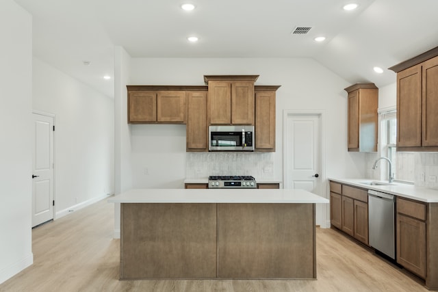 kitchen featuring appliances with stainless steel finishes, light wood-type flooring, a kitchen island, and vaulted ceiling