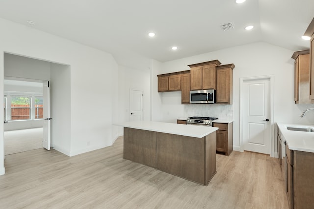 kitchen with appliances with stainless steel finishes, lofted ceiling, a center island, light hardwood / wood-style flooring, and sink