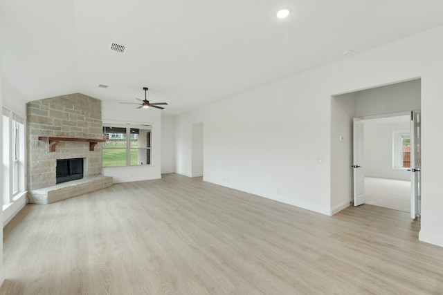 unfurnished living room with ceiling fan, a stone fireplace, and light wood-type flooring