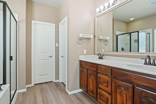 bathroom featuring a shower with shower door, wood-type flooring, and dual bowl vanity