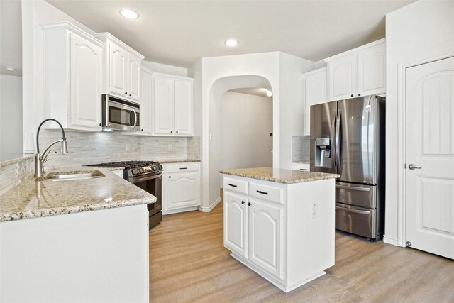 kitchen with white cabinets, decorative backsplash, sink, appliances with stainless steel finishes, and light hardwood / wood-style flooring