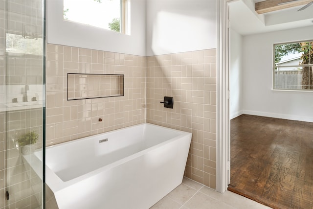 bathroom featuring tile walls, a bathing tub, a wealth of natural light, and tile patterned floors