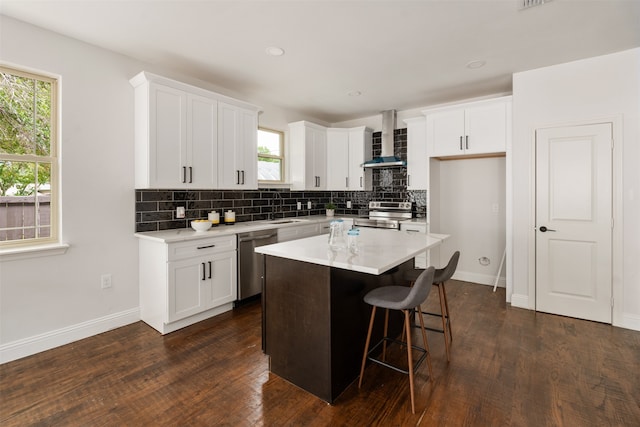 kitchen featuring appliances with stainless steel finishes, backsplash, a center island, white cabinetry, and wall chimney exhaust hood