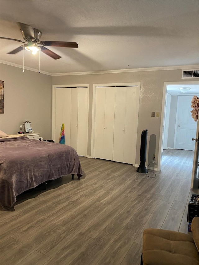 bedroom with multiple closets, crown molding, hardwood / wood-style floors, and ceiling fan