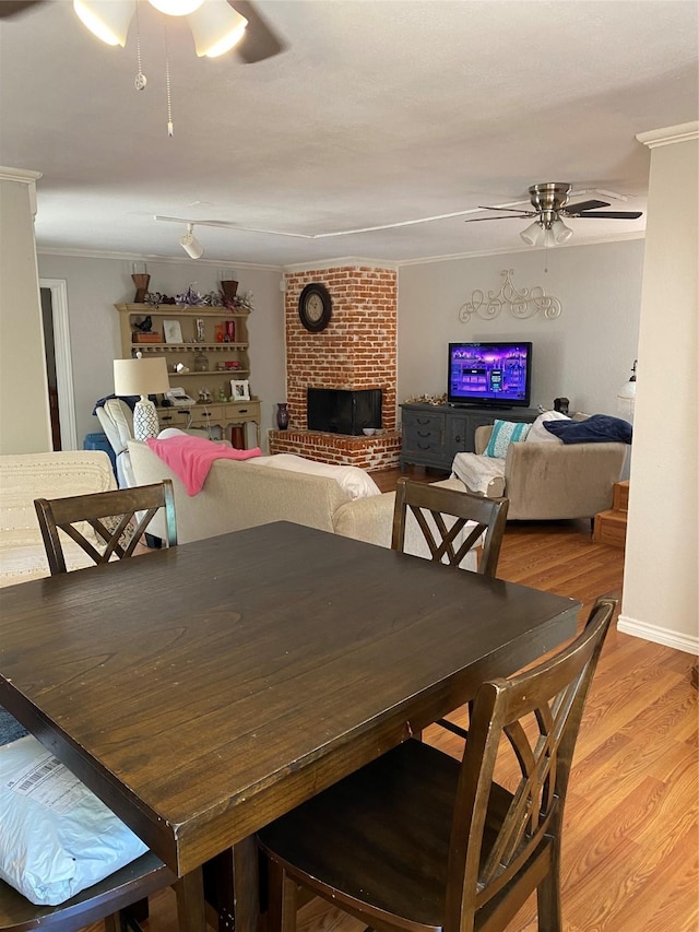 dining space with a brick fireplace, crown molding, light hardwood / wood-style flooring, and ceiling fan