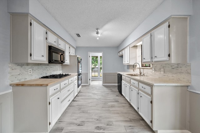 kitchen with white cabinetry, backsplash, black appliances, and light hardwood / wood-style flooring