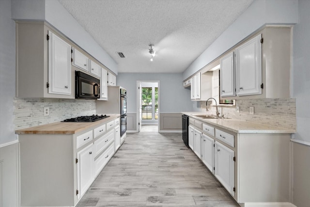 kitchen with butcher block counters, sink, white cabinetry, light hardwood / wood-style floors, and black appliances