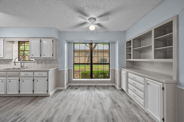 unfurnished dining area featuring ceiling fan, sink, a textured ceiling, and light wood-type flooring