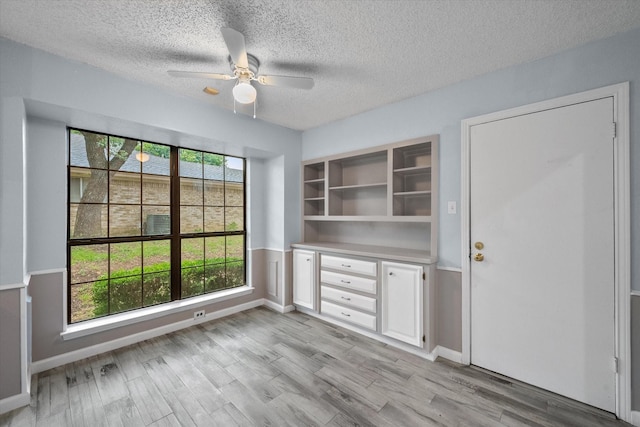 unfurnished dining area with ceiling fan, a textured ceiling, and light hardwood / wood-style floors