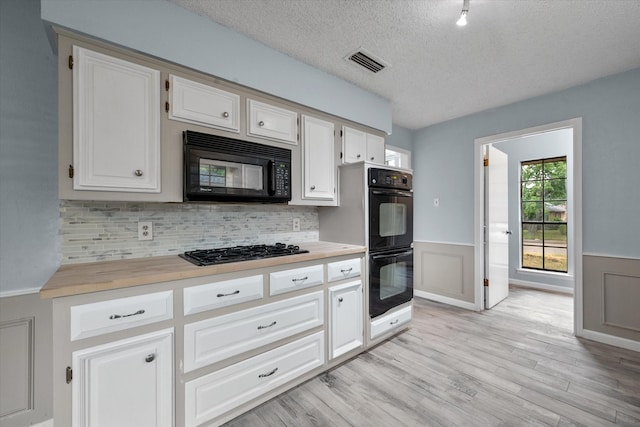 kitchen with white cabinetry, black appliances, decorative backsplash, light hardwood / wood-style floors, and a textured ceiling