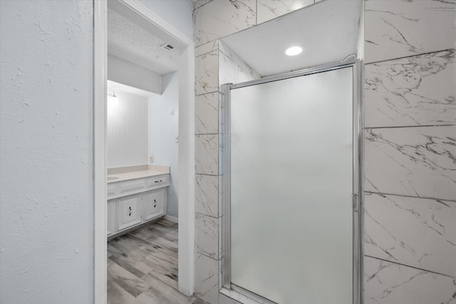 bathroom with vanity, an enclosed shower, a textured ceiling, and hardwood / wood-style floors