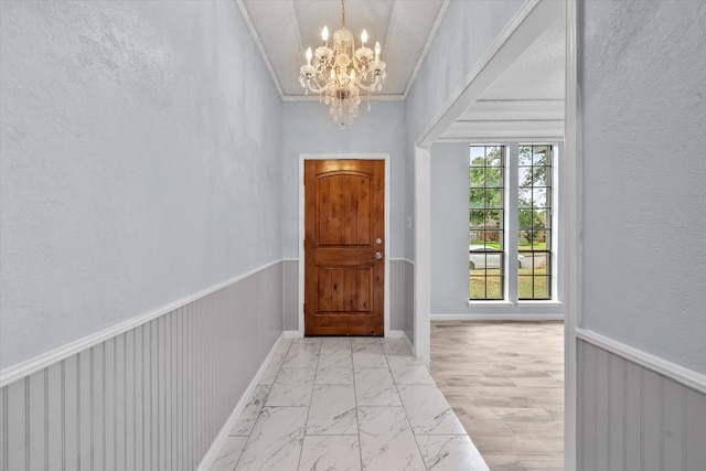 entryway with light wood-type flooring, a notable chandelier, ornamental molding, and a textured ceiling