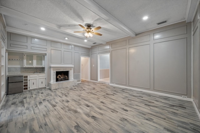 unfurnished living room with a premium fireplace, light wood-type flooring, ceiling fan, and a textured ceiling