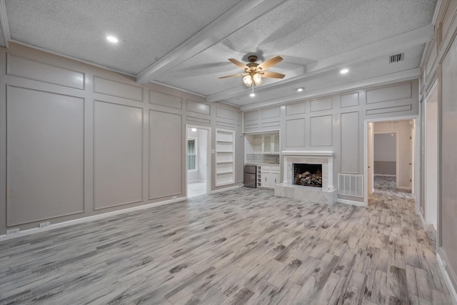 unfurnished living room with beamed ceiling, a high end fireplace, a textured ceiling, and light hardwood / wood-style flooring