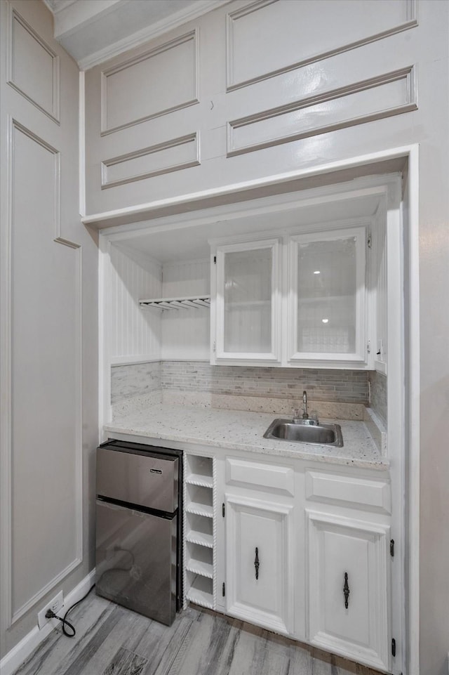 interior space with stainless steel refrigerator, sink, backsplash, white cabinets, and light stone countertops