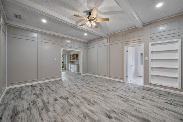 unfurnished living room featuring built in shelves, light hardwood / wood-style floors, a textured ceiling, and beamed ceiling