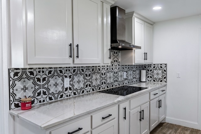 kitchen with decorative backsplash, light stone countertops, black electric cooktop, wood-type flooring, and wall chimney exhaust hood