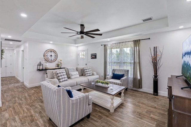 living room featuring hardwood / wood-style flooring, ceiling fan, and a tray ceiling