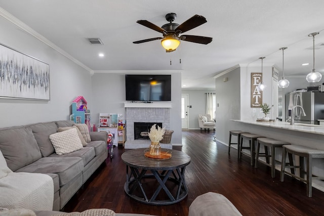 living room with sink, dark hardwood / wood-style flooring, ornamental molding, ceiling fan, and a brick fireplace