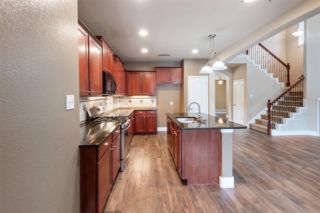 kitchen featuring hardwood / wood-style floors, a kitchen island with sink, stainless steel range with gas cooktop, sink, and ceiling fan