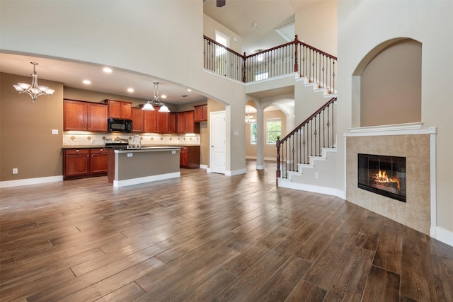 unfurnished living room featuring a high ceiling, dark hardwood / wood-style floors, a notable chandelier, and a tiled fireplace