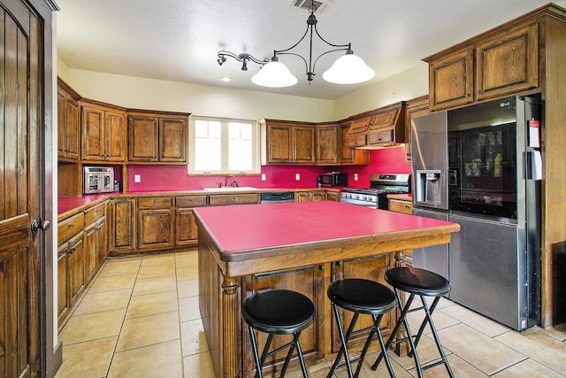 kitchen featuring a sink, a center island, light tile patterned floors, and stainless steel appliances