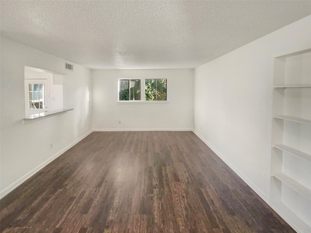 empty room with built in features, a textured ceiling, and dark hardwood / wood-style floors