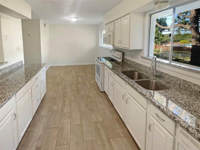 kitchen with white cabinetry, light stone countertops, white appliances, and sink