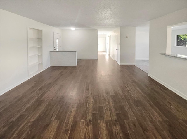 unfurnished living room featuring built in shelves, dark hardwood / wood-style flooring, and a textured ceiling