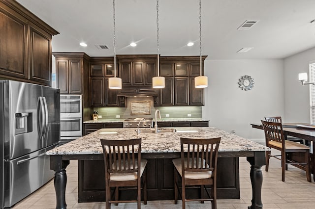 kitchen with pendant lighting, stainless steel appliances, sink, a center island with sink, and dark brown cabinets