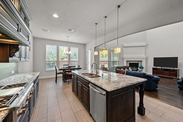 kitchen with an inviting chandelier, a kitchen island with sink, a fireplace, stainless steel dishwasher, and sink