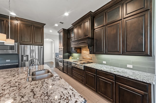 kitchen featuring light stone countertops, appliances with stainless steel finishes, decorative light fixtures, sink, and dark brown cabinets