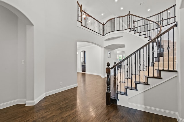 staircase with wood-type flooring and a towering ceiling