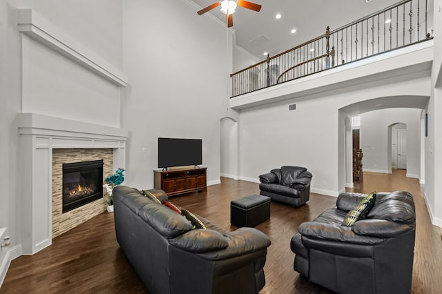 living room with ceiling fan, dark hardwood / wood-style floors, a tile fireplace, crown molding, and a high ceiling