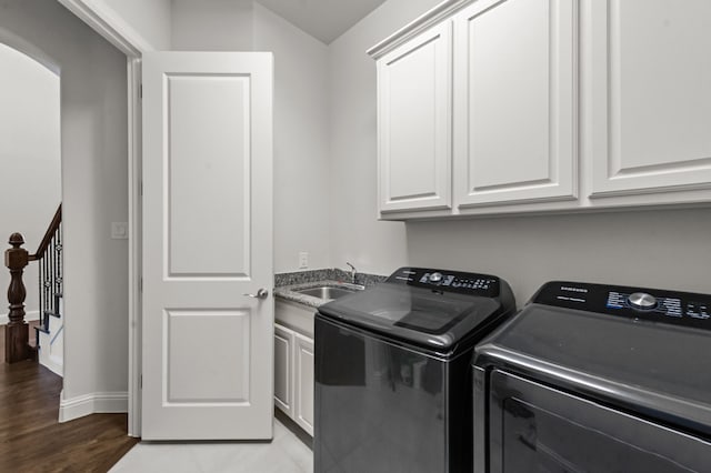 laundry area featuring wood-type flooring, sink, washing machine and clothes dryer, and cabinets