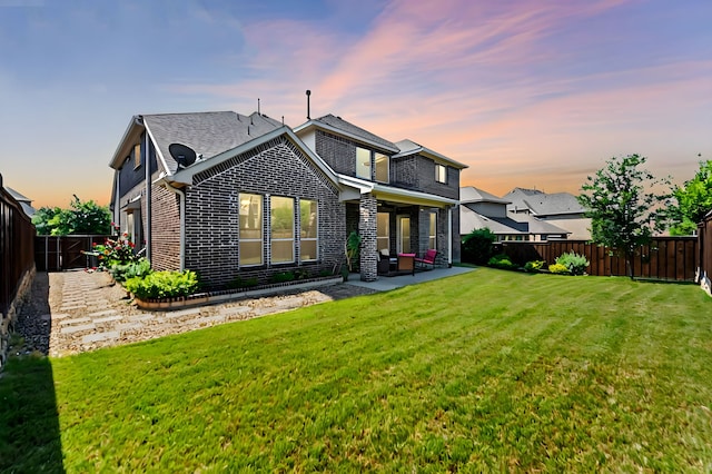 back house at dusk with a lawn and a patio