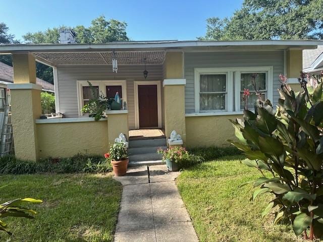 view of front of property with a porch, a front yard, and stucco siding