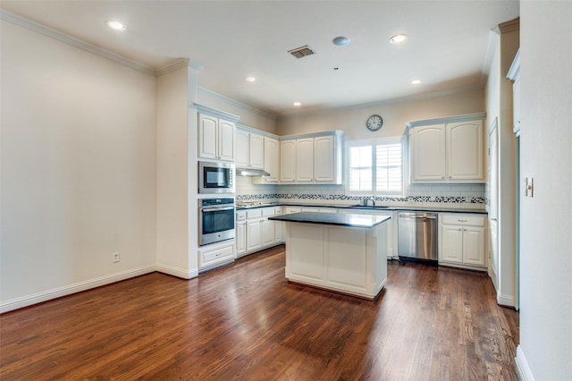 kitchen with appliances with stainless steel finishes, backsplash, white cabinets, a kitchen island, and dark hardwood / wood-style flooring