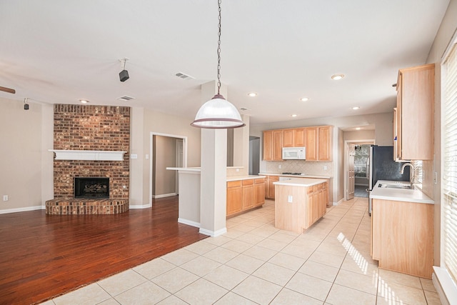 kitchen featuring light wood-type flooring, light brown cabinets, pendant lighting, a fireplace, and a kitchen island