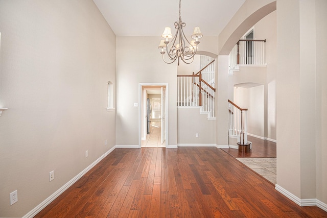 unfurnished living room with hardwood / wood-style flooring, a notable chandelier, and a towering ceiling