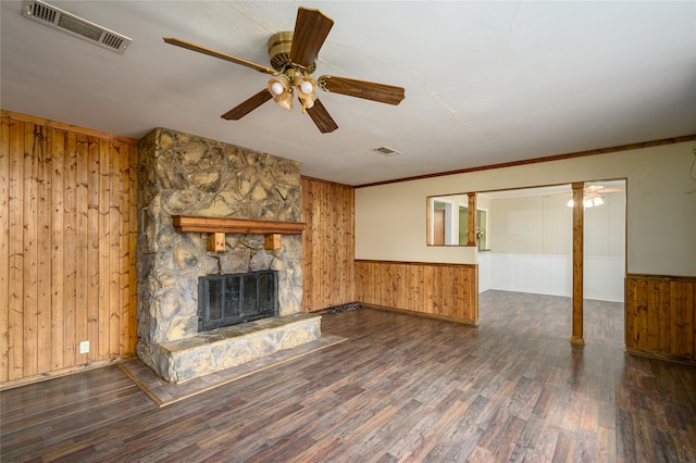 unfurnished living room featuring ceiling fan, dark hardwood / wood-style flooring, wooden walls, and a stone fireplace