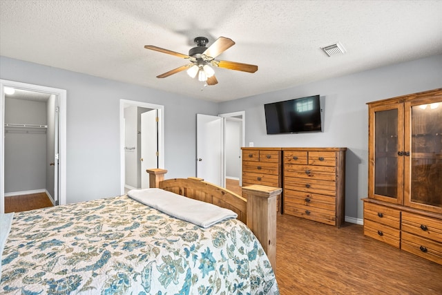 bedroom featuring a closet, hardwood / wood-style floors, a textured ceiling, a walk in closet, and ceiling fan