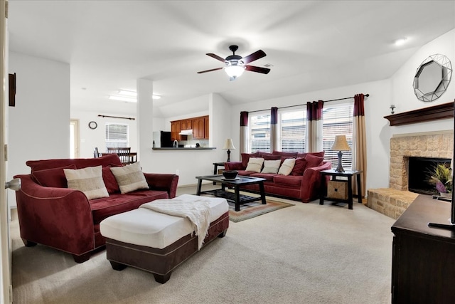 living room featuring ceiling fan, a stone fireplace, and light carpet