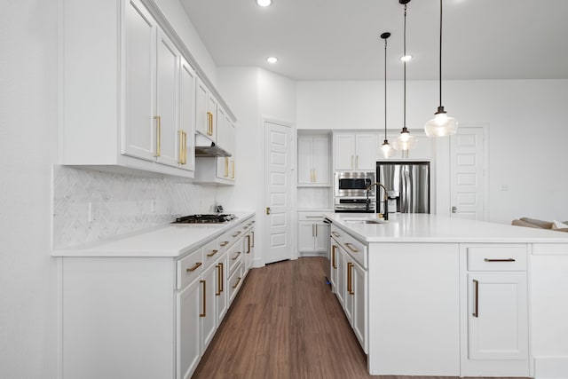 kitchen featuring an island with sink, appliances with stainless steel finishes, backsplash, decorative light fixtures, and white cabinets