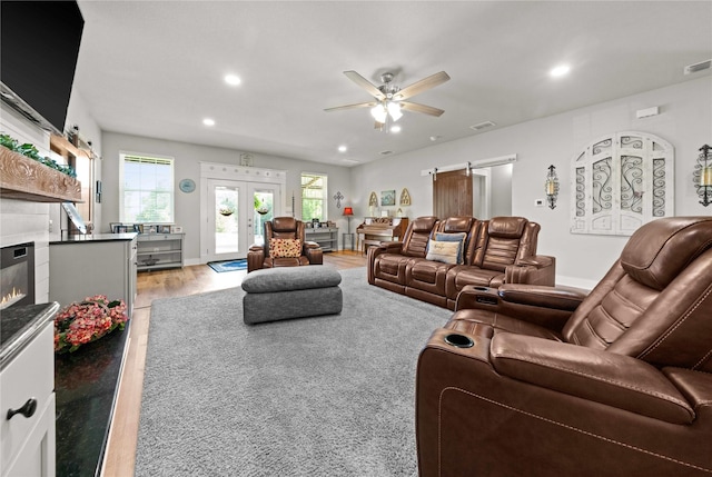 living room featuring french doors, ceiling fan, a barn door, and light hardwood / wood-style flooring