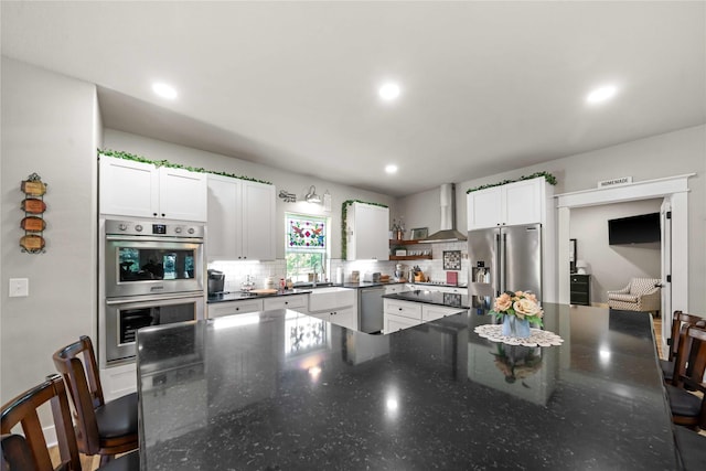 kitchen with wall chimney exhaust hood, a breakfast bar area, tasteful backsplash, appliances with stainless steel finishes, and white cabinets