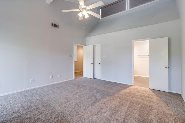 unfurnished bedroom with carpet flooring, ceiling fan, a spacious closet, a towering ceiling, and a closet