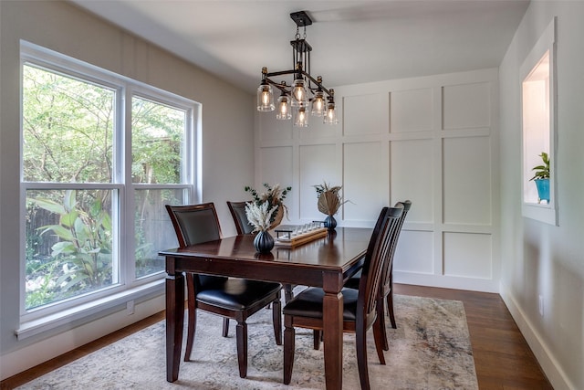 dining area with dark wood finished floors, a decorative wall, baseboards, and an inviting chandelier