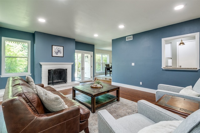 living room featuring a fireplace, french doors, a healthy amount of sunlight, and hardwood / wood-style floors