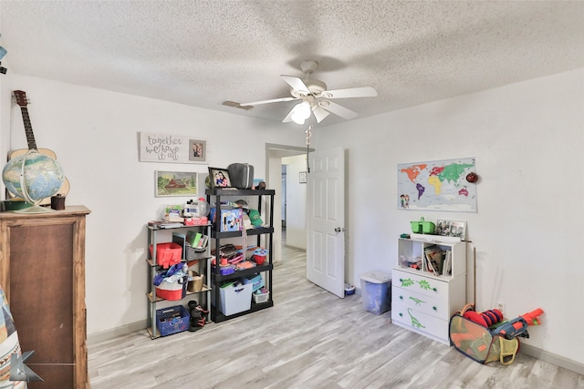 game room with a textured ceiling, ceiling fan, and light wood-type flooring